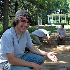Colour photograph of a young trainee archaeologist holding an arrow in his hand.