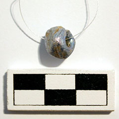 Photographie couleur d'une perle bleue facettée, en verre, sur un fil.