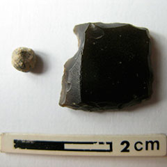 Photographie couleur d'une pierre à fusil en silex noir et d'une balle de fusil en plomb.