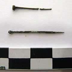 Colour photograph of two rusty copper needles. One is broken up in two parts, the other one is intact.