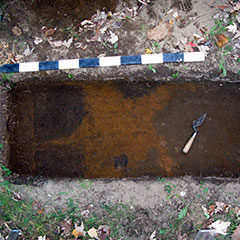 Colour photograph of a ground layer with a reddened area and of a trowel.