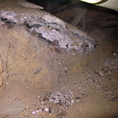 Photographie couleur d'un niveau de sol où l'on retrouve du bois incendié, de la cendre et des résidus variés.