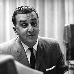 Photographie noir et blanc d'un homme bien rasé avec les cheveux peignés vers l'arrière, vêtu d'un costume et d'une cravate.