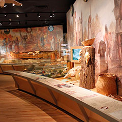 Photographie couleur d'une salle d'exposition où on retrouve plusieurs objets appartenant à la culture matérielle des Wôbanaki ainsi que des vidéos.