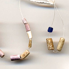 Photographie couleur de perles de coquillage blanches et violettes enfilées sur un fil.