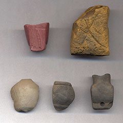 Photographie couleur de cinq fragments de pipes en pierre de couleurs et formes différentes.