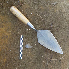 Colour photograph of an arrowhead next to a trowel.