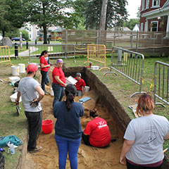 Photographie couleur des membres de l'équipe d'archéologie, certains sont debouts, d'autres creusent le sol.