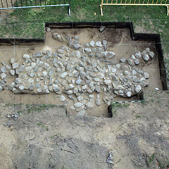 Colour photograph of an aerial view of several squared stones, forming a housing foundation. Strings placed vertically and horizontally are forming squares on the ground level.