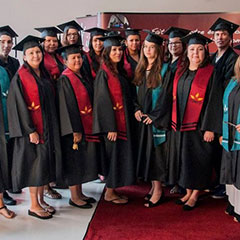 Colour photograph of twenty students during their graduation ceremony. They are all wearing a gown with a red or green scarf and a mortarboard.