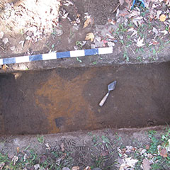 Photographie couleur d'une truelle et d'un sondage archéologique de traces de bois, le sol est rougi.
